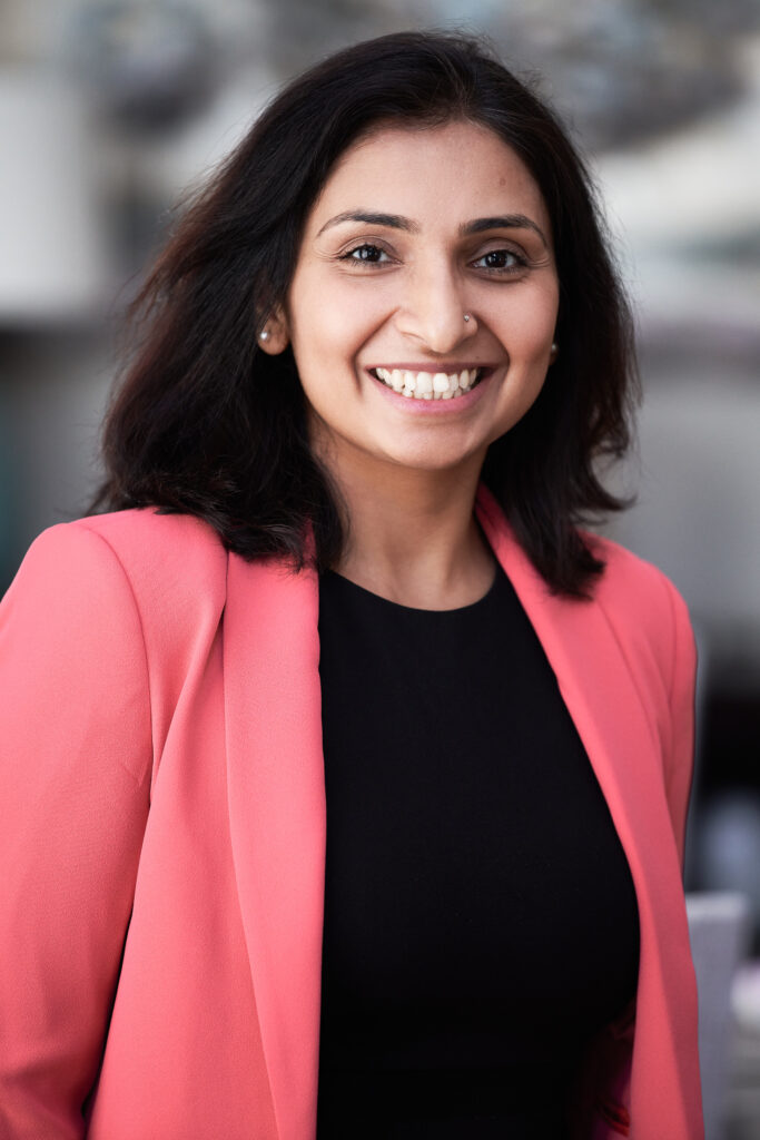 Portrait of Dr. Oberoi smiling and wearing a pink blazer with a black shirt underneath.