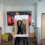 Meaghan & Amanda standing inside a carboard picture frame made to look covered in frosting. It says "Team Spirit, Frosting, & Fun!"